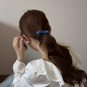 Detail showing a blue fabric double-layered bow hair tie on a model with a low ponytail.