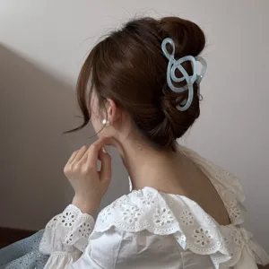 Vista detallada de una pinza de pelo azul con forma de nota musical en un moño elegante.