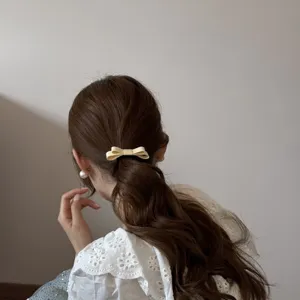 Detailed view of a small cream fabric double-layer bow hair tie styled in a low ponytail