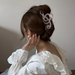 Detalle de una pinza para el pelo rosa con forma de clave de sol en un moño elegante