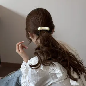 Detail view of a cream double-layered fabric bow hair tie on a wavy low ponytail.