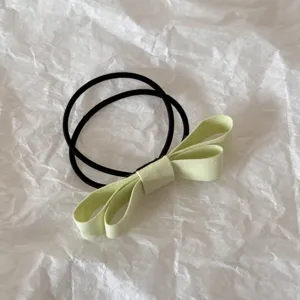 Detailed close-up of a light green fabric bow hair tie on a white textured paper background