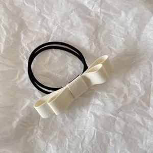 Close-up of an elegant double-layered cream fabric bow hair tie on textured paper