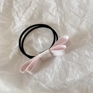 Close-up detail of a light pink fabric double bow hair tie on white background.