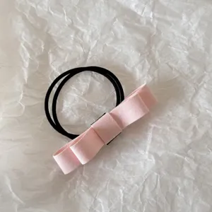 Detailed view of a pink fabric bow hair tie with double-strand black elastic band