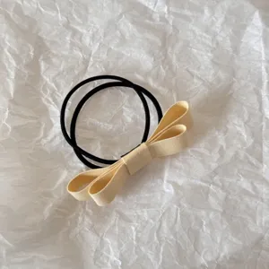Detailed close-up view of a minimalist cream fabric bow hair tie on a white textured background