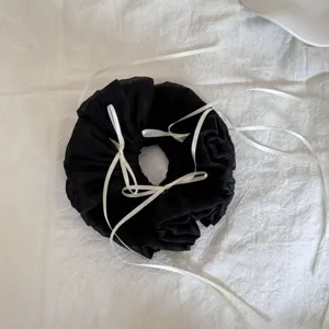 Detailansicht eines schwarzen Mesh-Scrunchies mit weißen Schleifenverzierungen.