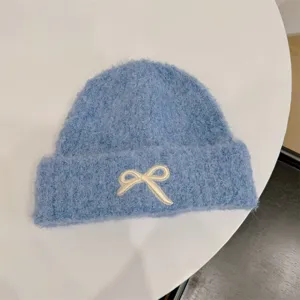 Detail view of a cozy light blue knit beanie featuring a cute white ribbon embroidery