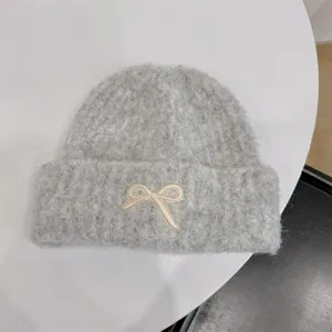 Detail of a grey knitted beanie featuring a cream bow applique on a white table