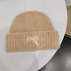 Detailed macro view of the white bow embroidery on a beige fuzzy knit winter beanie hat