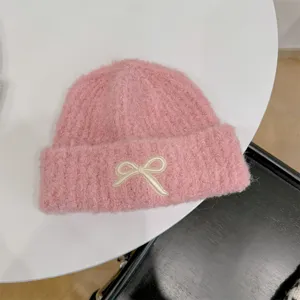 Detailed view of soft pink knit beanie featuring a cute embroidered cream bow detail