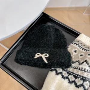 Close-up of a black textured knit beanie featuring a white bow detail decoration.