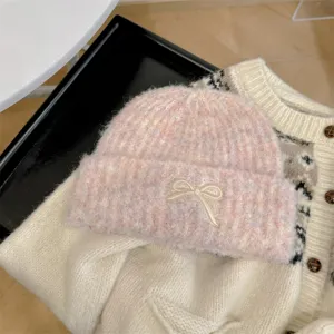 Detail view of a pink marbled knitted beanie with a cute cream bow embroidery.