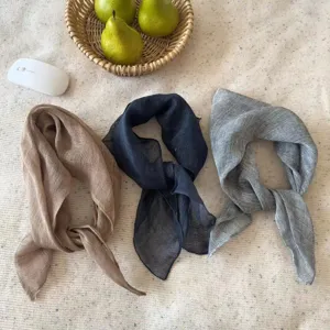 Macro view of three breathable pure linen square scarves in tan, navy, and grey tones.