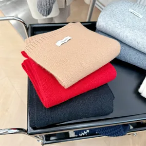 Close-up detail of premium 100% wool knitted scarves stacked in camel, red and black colors