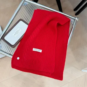 Detailweergave van rode ribgebreide sjaal met decoratieve schelpknoop