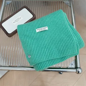 Detailweergave van een groene gebreide sjaal met een schelpknoop en handgemaakt label.