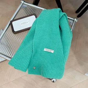 Detailopname van een groene wollen sjaal met decoratieve schelpknoop en geweven label.