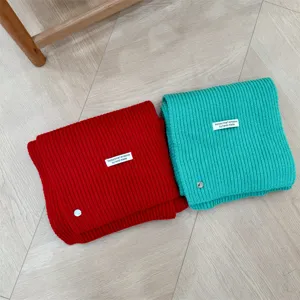 Detailopname van gebreide wollen sjaals in rood en groen met schelpknopdetail