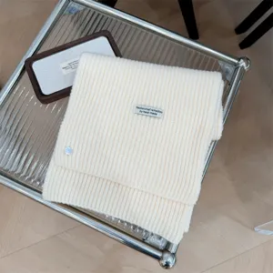 Detail van een crème gebreide sjaal met decoratieve schelpknoop en handgemaakt label.