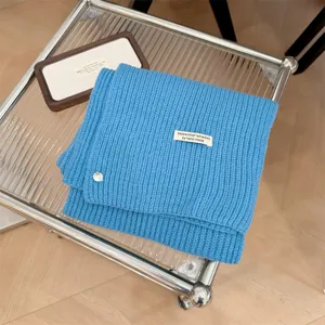Gedetailleerd aanzicht blauwe gebreide sjaal met schelpknoop en handgemaakt label