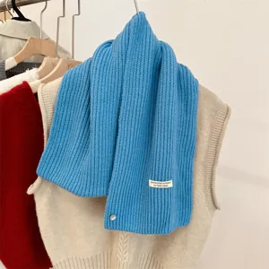 Detail van een wollen gebreide sjaal met decoratieve schelpknoop en label