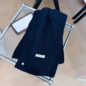 Detail van een marineblauwe wollen sjaal met label en een knoop van schelpmateriaal
