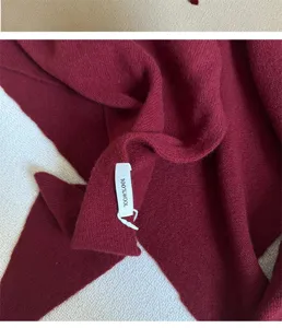 Makroaufnahme des 100% Wolle-Etiketts auf einem weichen weinroten Strickschal-Detail
