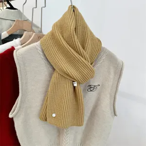 Detailopname van een camelkleurige wollen gebreide sjaal met een decoratieve witte schelpknoop