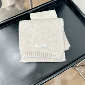 Detailed view of a premium 100% wool beige knitted scarf texture and sewn label on a tray.