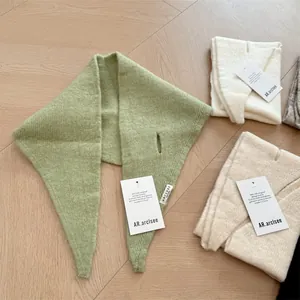 Detailed view of multiple soft wool knit triangular scarves in green and beige.