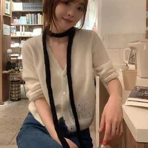 Gros plan d'une écharpe longue en maille noire portée avec un cardigan blanc