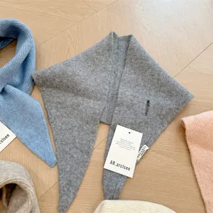 Close-up of a grey wool blend knit triangle scarf with brand tag and knit texture detail