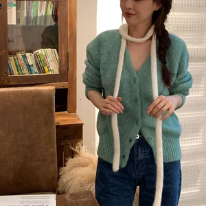Gros plan d'une longue écharpe blanche en tricot caterpillar portée avec un cardigan vert