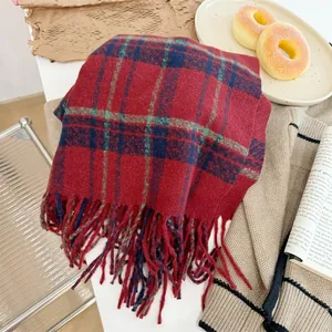 Gros plan d'une écharpe à carreaux rouge vintage avec pompons dans un décor d'hiver douillet.