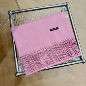 Elegante bufanda pashmina rosa con flecos mostrada sobre una mesa de cristal