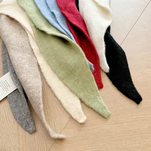 Detail view showing various colors of wool-blend knitted triangular scarves on a wooden surface