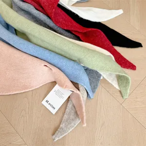 Detailed view of assorted colors wool knit triangle scarves with brand label on wood