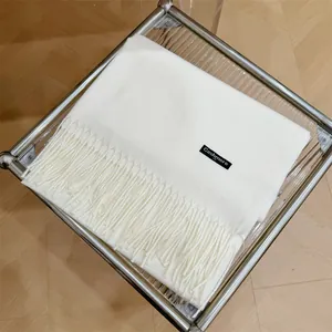 Vista detallada de una bufanda de cachemira crema con flecos sobre mesa de cristal