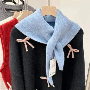 Detailed shot of a light blue wool blend knitted triangular scarf with pink bow accents.