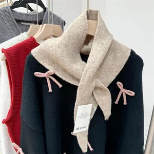 Detail view of a beige wool knit triangle scarf with brand tag over a black sweater