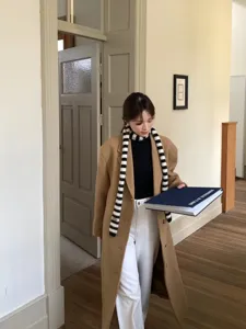 Bufanda larga de punto a rayas blancas y negras llevada por una modelo en un interior.