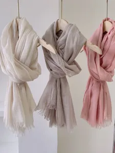 Dettaglio di sciarpe leggere in cotone e lino in beige, talpa e rosa su stampelle