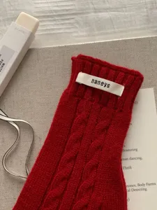 Dettaglio di un guanto rosso in maglia a trecce senza dita con etichetta del brand