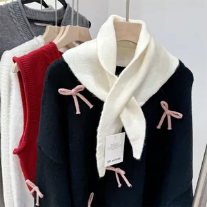 Close-up view of a cream wool knit triangle scarf paired with a black bow-detail sweater.