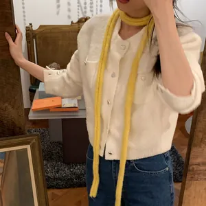 Gros plan d'une écharpe en maille chenille jaune vif portée avec un cardigan blanc douillet