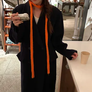 Vue détaillée d'une écharpe en tricot orange vif portée avec un manteau sombre