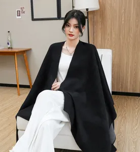 Elegant black knitted shawl cloak draped over a model in a cozy indoor office setting