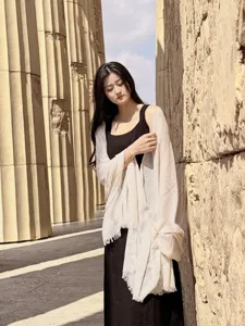Dettaglio di uno scialle in lino beige indossato da una modella in rovine soleggiate