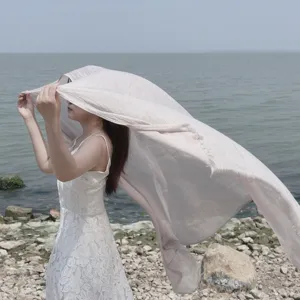 Elegante scialle beige in cotone e lino che soffia nel vento sugli scogli del mare